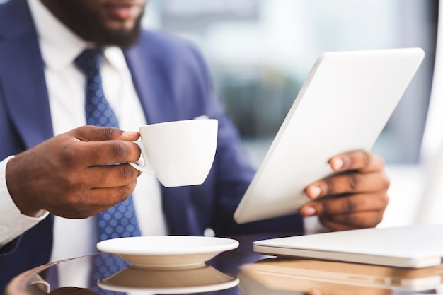 Uomo d'affari afroamericano irriconoscibile che mangia caffè mentre lavora al tablet