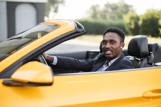 Uomo d'affari afroamericano maturo seduto nel veicolo sportivo di lusso e sorridente guardando da parte