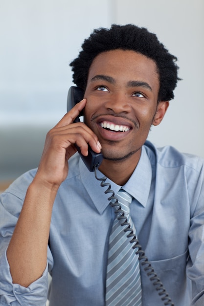 Uomo d&#39;affari afroamericano sorridente attraente sul telefono in ufficio