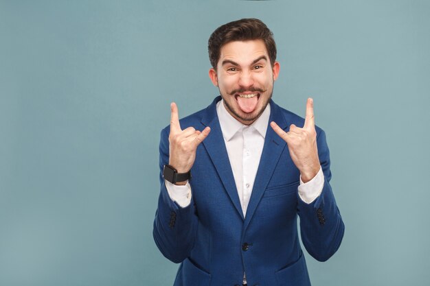 Uomo d'affari aggressivo con la lingua fuori e mostra il segno del rock and roll