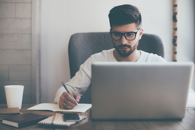 Uomo d'affari al lavoro. Giovane fiducioso che scrive qualcosa sul taccuino mentre è seduto al suo posto di lavoro in ufficio