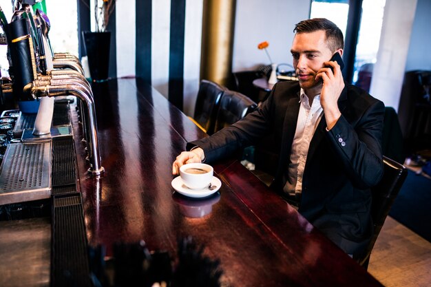 Uomo d&#39;affari al telefono con un caffè al bancone in un bar