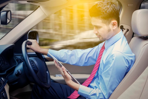 Uomo d'affari alla guida di un'auto durante l'utilizzo del tablet