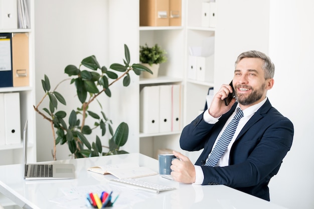 Uomo d'affari allegro che comunica sul telefono cellulare