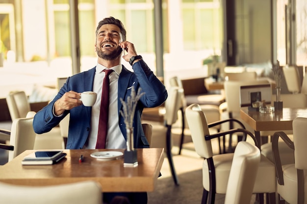 Uomo d'affari allegro che parla al telefono mentre fa una pausa caffè in un caffè