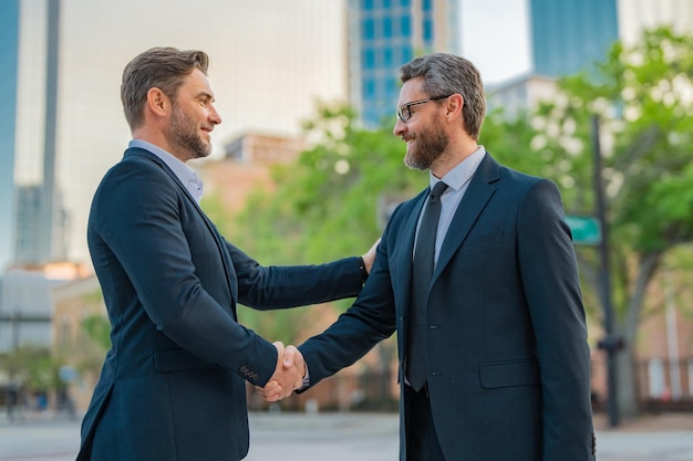 Uomo d'affari americano che stringe la mano a uomini d'affari partner in tuta che stringe la mano all'aperto affari