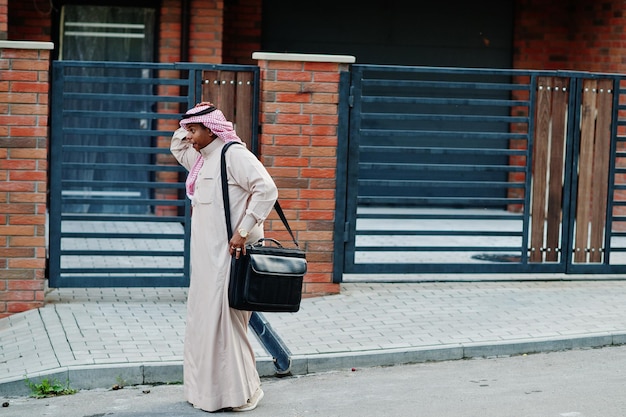 Uomo d'affari arabo mediorientale posato su strada contro un edificio moderno con borsetta nera