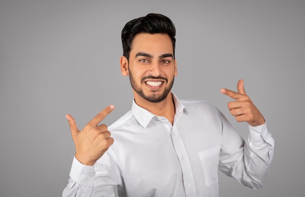 Uomo d'affari arabo sorridente che punta il dito contro se stesso e guarda l'obbiettivo