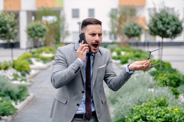 Uomo d'affari arrabbiato nell'usura convenzionale che urla sopra lo Smart Phone sul suo impiegato mentre stando all'aperto.