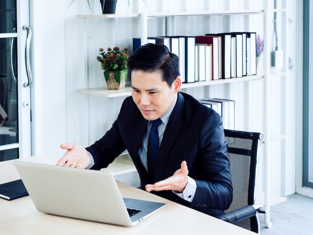 Uomo d'affari asiatico bello in videochiamata tuta, spiegando al collega tramite computer portatile in riunione di lavoro online, videoconferenza