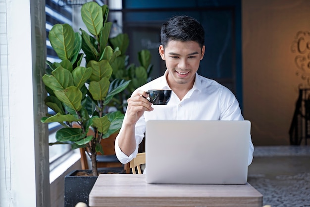 Uomo d'affari asiatico bello o impiegato che lavora alla caffetteria