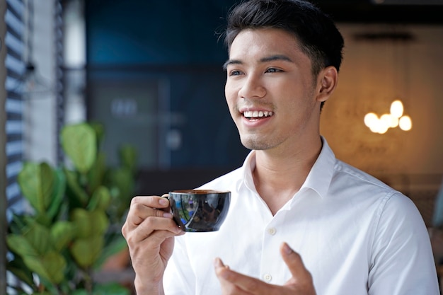 Uomo d'affari asiatico bello o impiegato o giovane studente che beve caffè al negozio di caffè