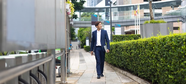 Uomo d'affari asiatico che indossa la giacca a piedi per andare a lavorare la mattina all'aperto.