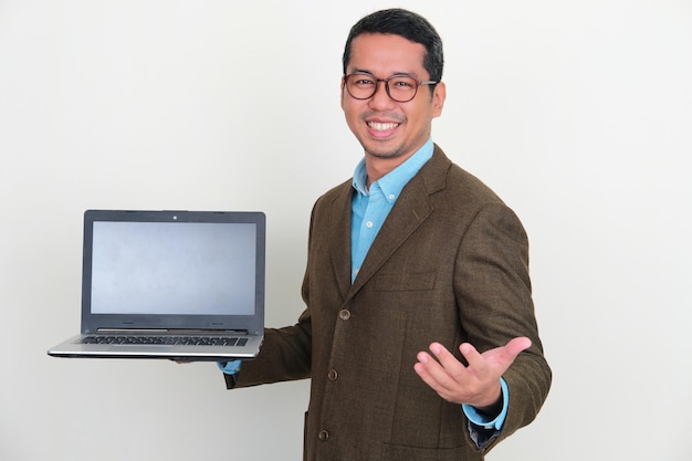 Uomo d'affari asiatico che mostra lo schermo del computer portatile vuoto con l'espressione felice