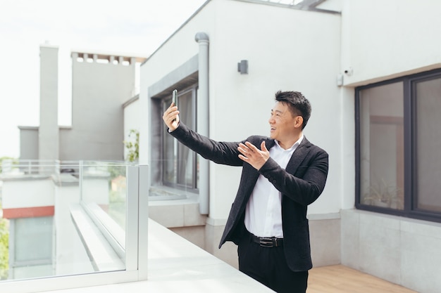 uomo d'affari asiatico che parla al videotelefono in piedi sul balcone terrazza balcony