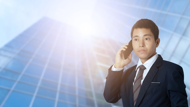 Uomo d'affari asiatico che parla smartphone fuori dall'ufficio in città urbana.