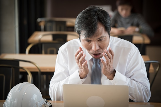 Uomo d&#39;affari asiatico con faccia sorpresa davanti al computer portatile.