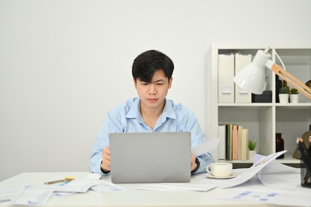 Uomo d'affari asiatico concentrato che controlla la posta elettronica o il marketing online sul computer portatile alla scrivania dell'ufficio
