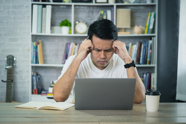 Uomo d'affari asiatico indossa gli occhiali e la mano sopra la testa con depressione stressante tempo triste mentre lavora sul portatile a casa depressione uomo triste serio lavorare da casa lavorare in qualsiasi luogo concetto