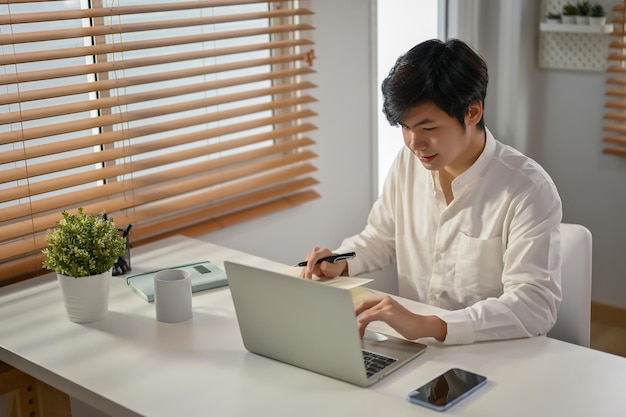 Uomo d'affari asiatico intelligente che lavora sui suoi compiti aziendali sul laptop nel suo spazio di lavoro
