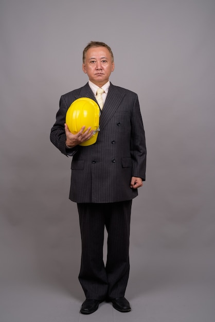 Uomo d'affari asiatico maturo della costruzione contro il muro grigio