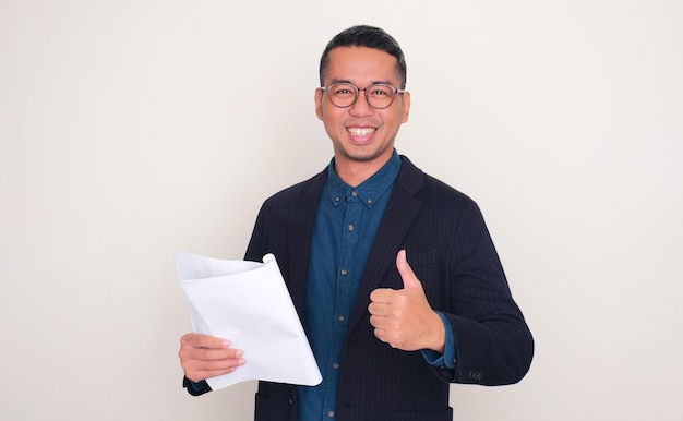 Uomo d'affari asiatico sorride felice e alza il pollice mentre tiene in mano un documento di relazione