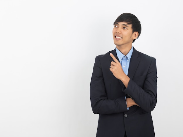 Uomo d'affari asiatico sorridente felice in vestito nero che indica lo spazio della copia isolato su fondo bianco, concetto di successo di affari