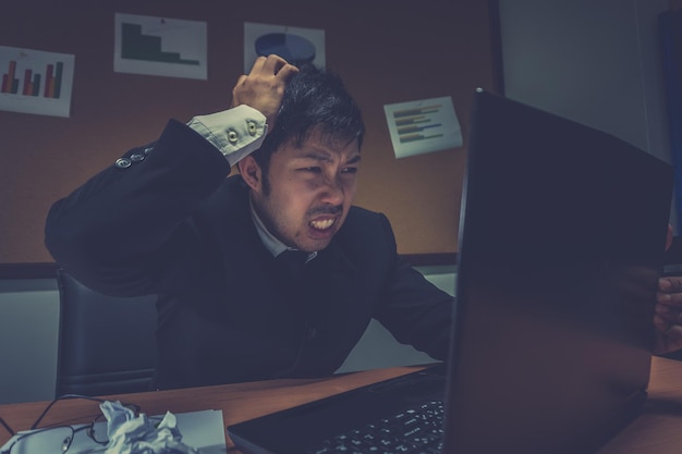 Uomo d'affari asiatico sotto stress a causa di un lavoro eccessivo Sentendosi esausto Il giovane impiegato ha un problema in un ufficioad uomo dal lavoro Concetto di uomo disordinato arrabbiato