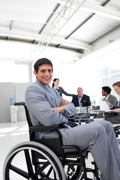 Uomo d&#39;affari attraente che si siede in una sedia a rotelle con le braccia piegate
