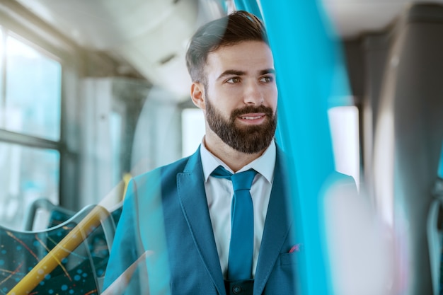 Uomo d'affari attraente sorridente dei giovani in vestito blu che si siede in bus e nel distogliere lo sguardo pubblici.