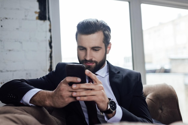 Uomo d'affari barbuto bello che utilizza smartphone