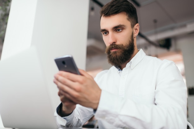 Uomo d'affari barbuto che per mezzo del computer portatile e dello smartphone