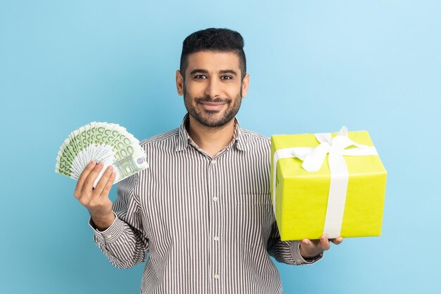 Uomo d'affari barbuto che tiene la scatola attuale avvolta e l'euro dei soldi che guarda l'obbiettivo sorridendo soddisfatto