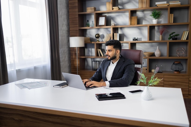 Uomo d'affari barbuto di successo in uit elegante che lavora su un computer portatile in un ufficio moderno