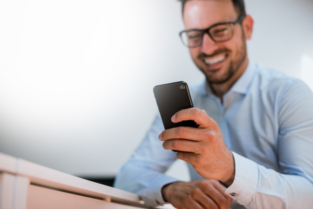 Uomo d&#39;affari barbuto felice che per mezzo del telefono mentre sedendosi nell&#39;ufficio.