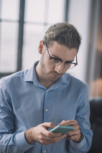 Uomo d'affari barbuto in camicia blu che osserva sul telefono