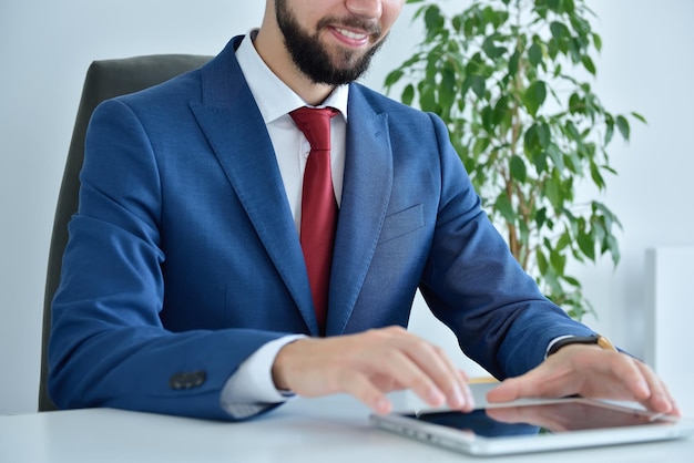 Uomo d'affari barbuto in giacca e cravatta utilizzando la tavoletta digitale in ufficio moderno