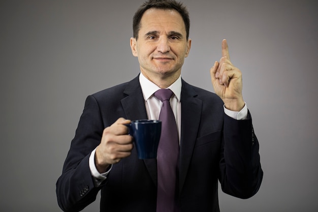 Uomo d'affari bello 40s con la tazza di caffè che sorride indicando sul suo indice