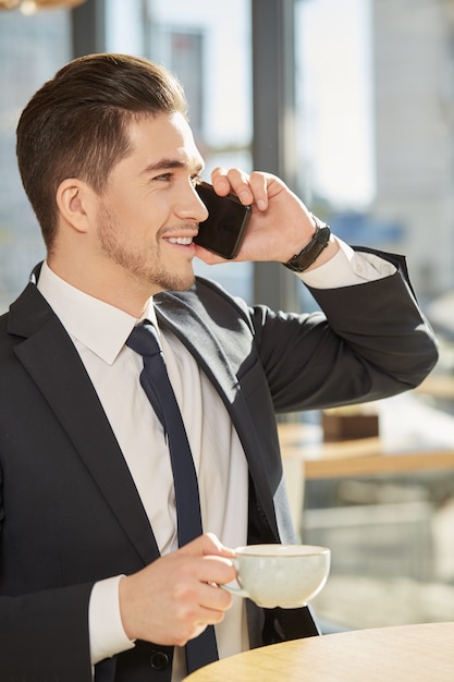 uomo d&#39;affari bello che gode del suo caffè che parla sul telefono che sorride felicemente