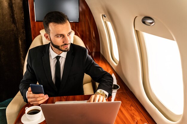 Uomo d'affari bello che porta vestito elegante che vola su un jet privato esclusivo