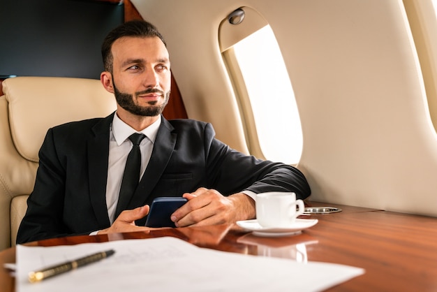 Uomo d'affari bello che porta vestito elegante che vola su un jet privato esclusivo