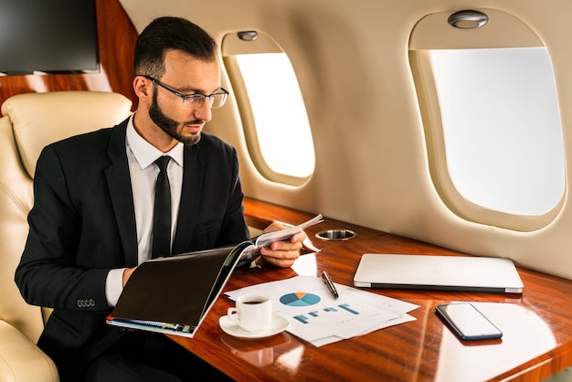 Uomo d'affari bello che porta vestito elegante che vola su un jet privato esclusivo