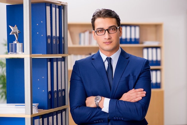 Uomo d&#39;affari bello che si leva in piedi vicino allo scaffale