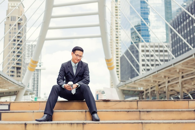 Uomo d'affari bello del giovane Asia che beve caffè caldo nella città moderna.