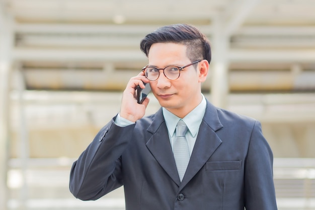 Uomo d&#39;affari bello del giovane Asia con il suo smartphone che sta sul passaggio pedonale della città moderna.