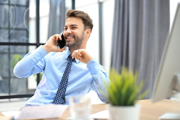 Uomo d'affari bello in ufficio che parla al telefono