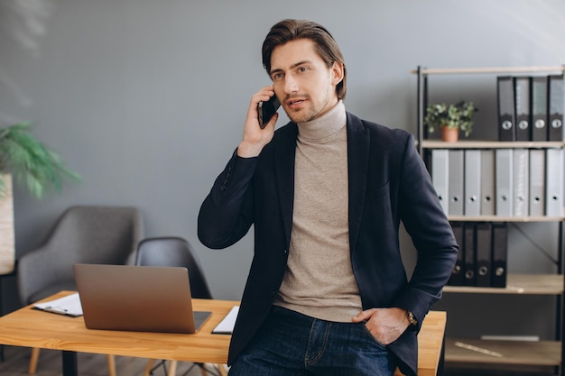 Uomo d'affari bello in vestito che parla al telefono nell'ufficio moderno