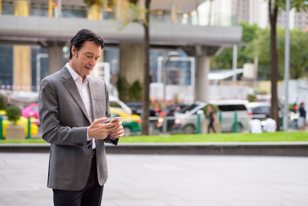 Uomo d'affari bello maturo utilizzando il telefono cellulare in città