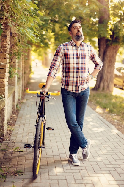 Uomo d'affari casual che va a lavorare in bicicletta. Sta camminando accanto alla bicicletta e sta pensando.