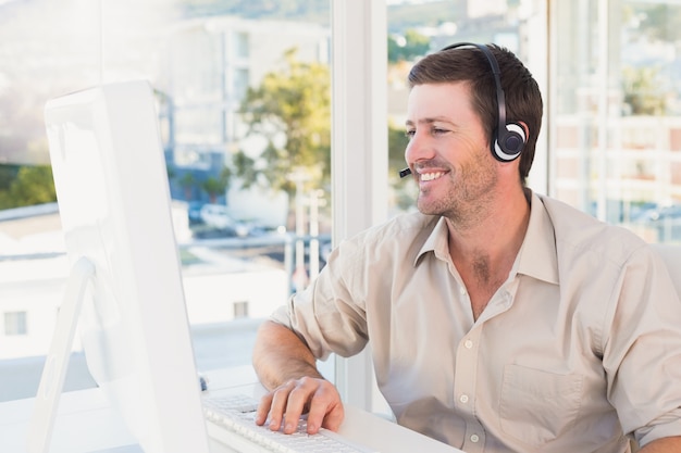 Uomo d&#39;affari casuale sorridente che ascolta il computer allo scrittorio